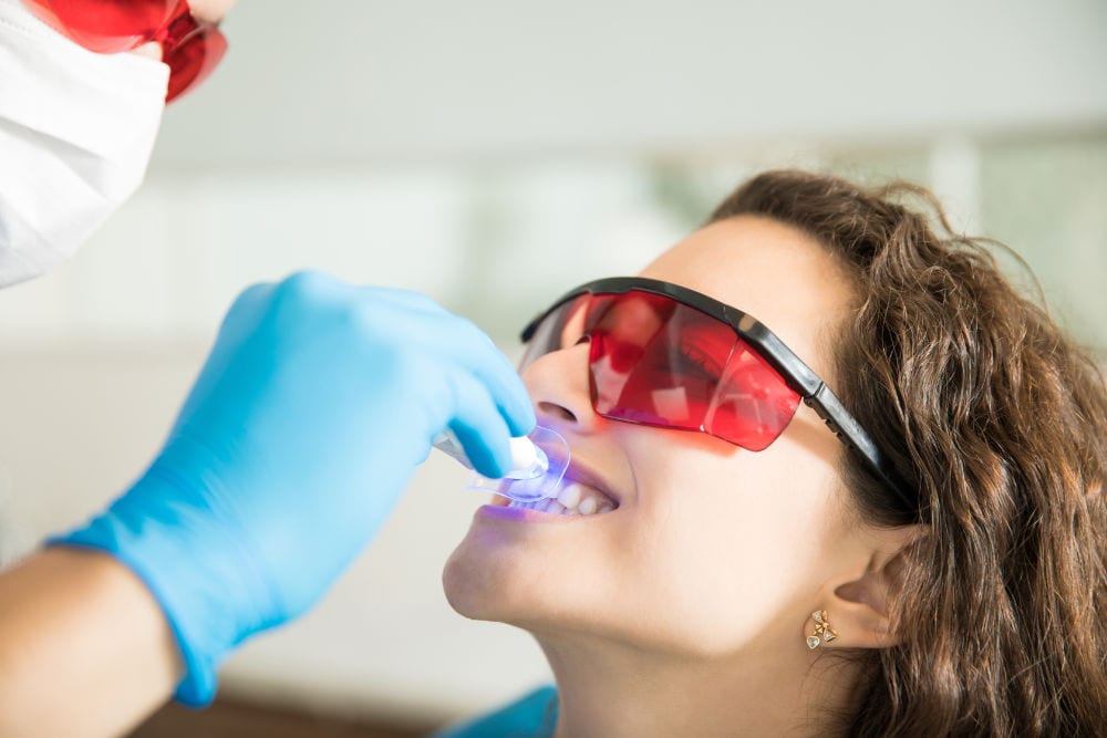 A patient having in-chair teeth whitening under a blue light